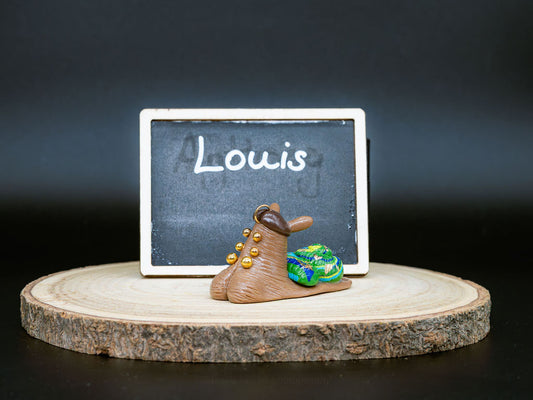 Small snail with piercings and a decorative shell on a wooden platform in front of a chalkboard with the name 'Louis' written on it